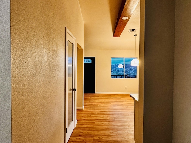 hallway with light wood-type flooring, a textured wall, and baseboards