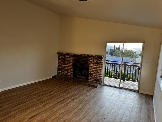 unfurnished living room featuring wood finished floors, baseboards, a brick fireplace, and vaulted ceiling