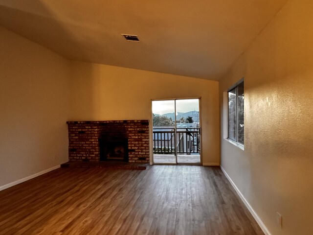 unfurnished living room featuring a mountain view, wood finished floors, baseboards, vaulted ceiling, and a fireplace