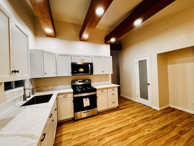kitchen featuring appliances with stainless steel finishes, a sink, beam ceiling, light stone countertops, and light wood finished floors