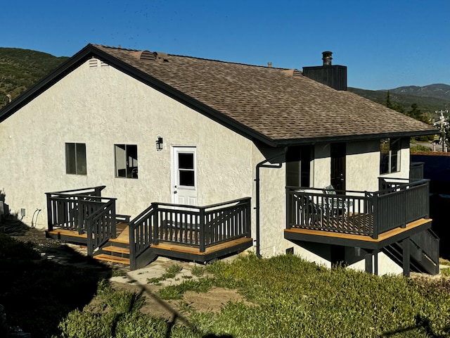 rear view of property with roof with shingles, a chimney, stucco siding, and a deck with mountain view