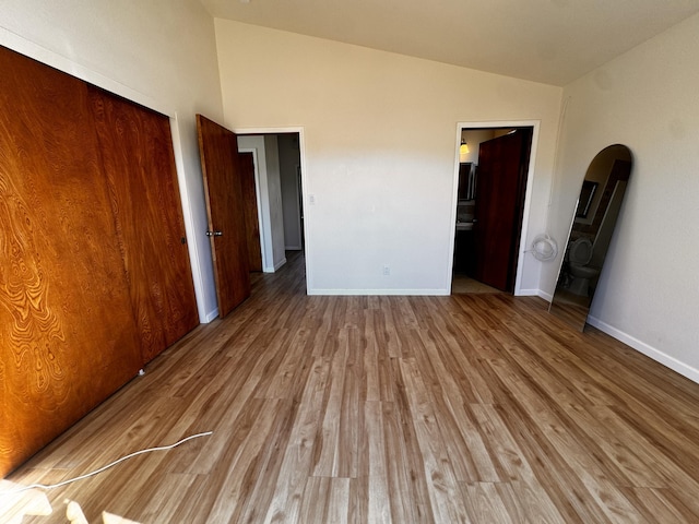 unfurnished bedroom with lofted ceiling, arched walkways, wood finished floors, baseboards, and a closet