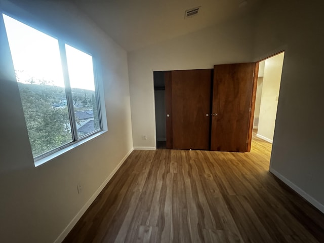 unfurnished bedroom featuring wood finished floors, baseboards, vaulted ceiling, and a closet