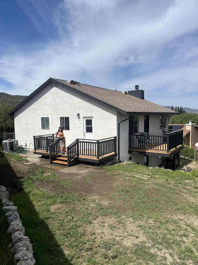rear view of house featuring a wooden deck, cooling unit, and a yard
