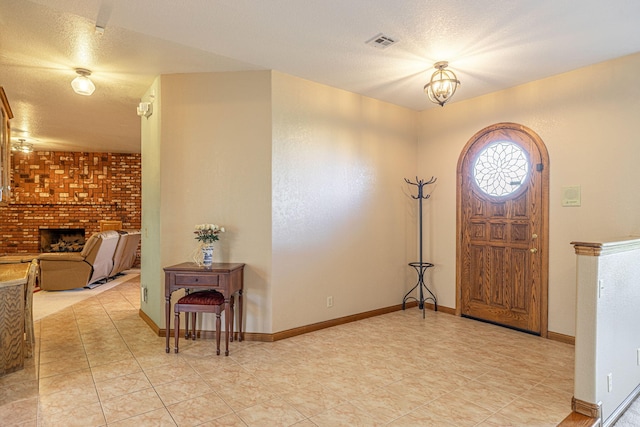 foyer featuring a chandelier, a textured ceiling, brick wall, and a brick fireplace