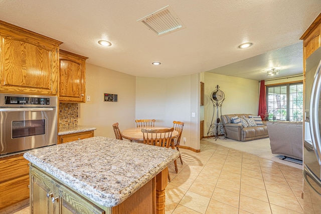 kitchen featuring light stone countertops, decorative backsplash, a textured ceiling, a center island, and oven