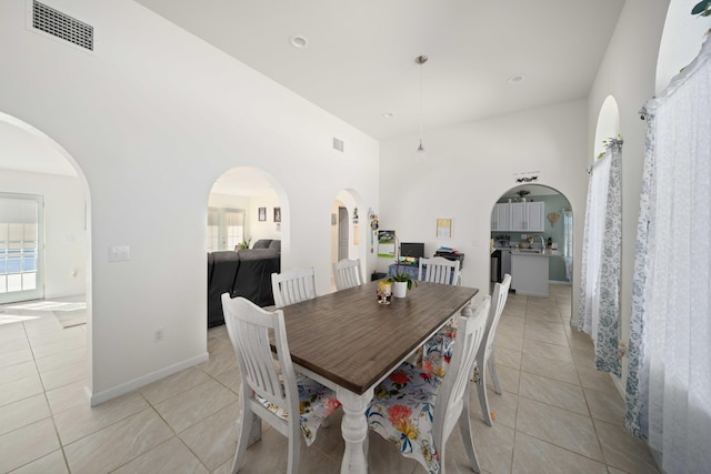 dining space featuring light tile patterned flooring, a towering ceiling, and sink