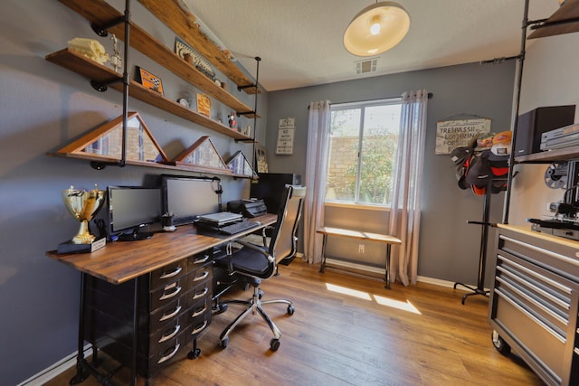office space with baseboards, visible vents, and wood finished floors