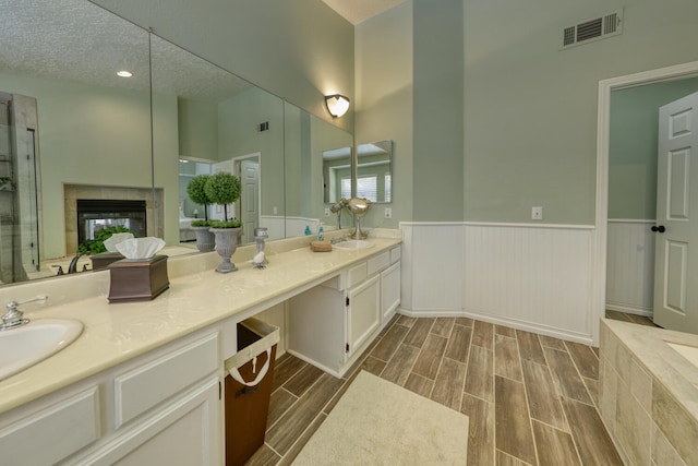 full bath with double vanity, visible vents, wainscoting, wood finished floors, and a sink