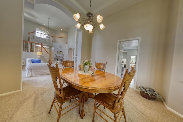 carpeted dining room featuring stairs, a towering ceiling, baseboards, a chandelier, and arched walkways