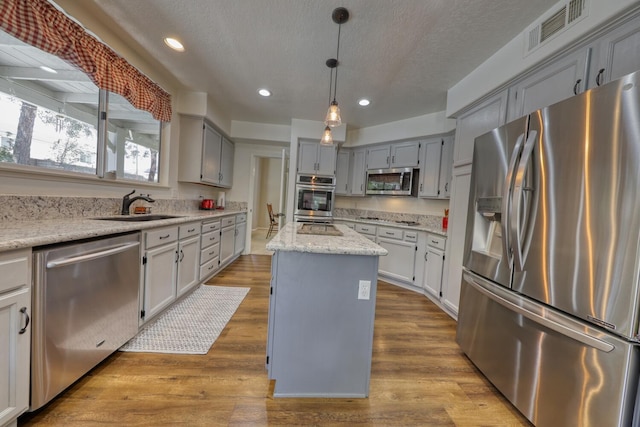 kitchen featuring gray cabinets, visible vents, appliances with stainless steel finishes, a center island, and a sink