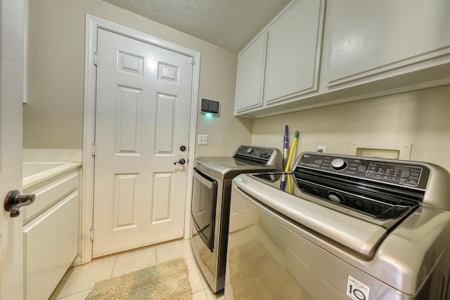 clothes washing area with washer and clothes dryer, cabinet space, a textured ceiling, and light tile patterned floors