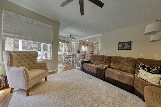 living room with a textured ceiling, ceiling fan, and light wood-style flooring