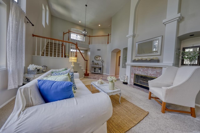 carpeted living room with a towering ceiling, baseboards, stairway, a high end fireplace, and a chandelier