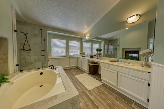 full bath with a multi sided fireplace, a garden tub, a textured ceiling, a stall shower, and vanity