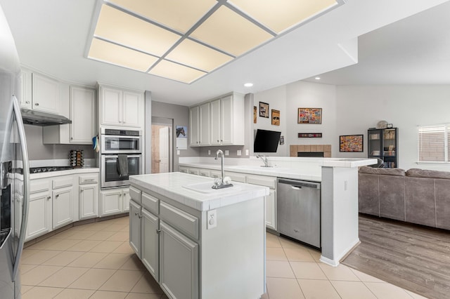 kitchen featuring a sink, open floor plan, a peninsula, appliances with stainless steel finishes, and tile counters