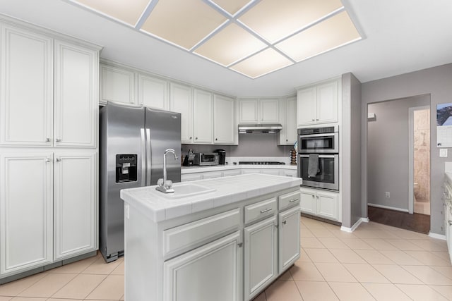 kitchen featuring a center island, under cabinet range hood, tile countertops, light tile patterned floors, and appliances with stainless steel finishes