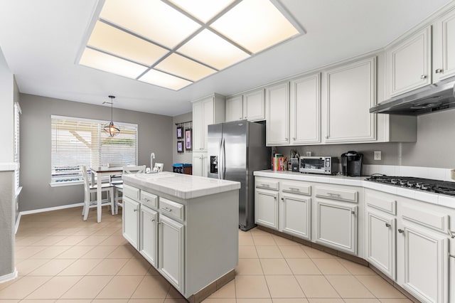 kitchen featuring under cabinet range hood, light tile patterned floors, tile countertops, and stainless steel fridge