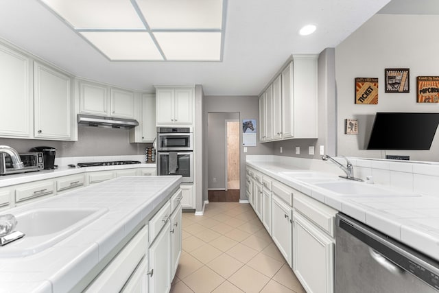 kitchen featuring tile countertops, white cabinets, under cabinet range hood, and stainless steel appliances