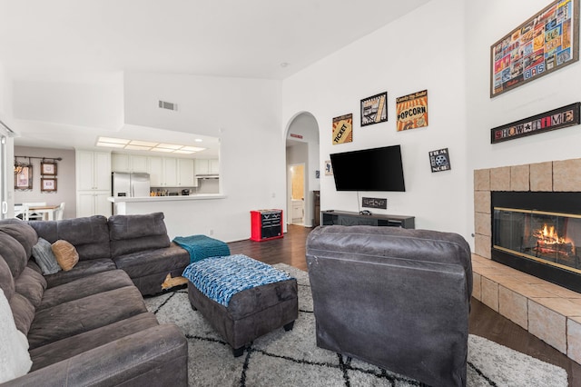 living room with visible vents, a tile fireplace, wood finished floors, arched walkways, and vaulted ceiling