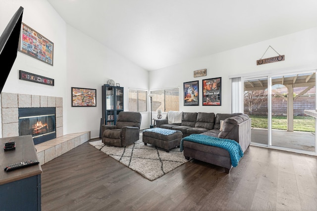 living room with a tiled fireplace, wood finished floors, and high vaulted ceiling