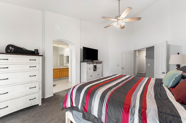 bedroom featuring dark carpet, a high ceiling, arched walkways, ensuite bath, and a ceiling fan