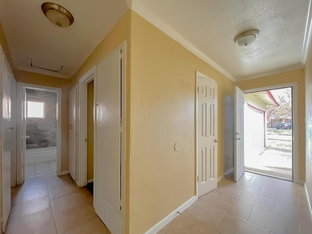 hall with light tile patterned floors, a textured ceiling, baseboards, attic access, and crown molding