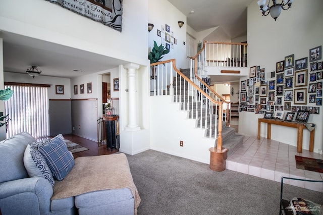 living room with baseboards, a towering ceiling, carpet, stairs, and ornate columns