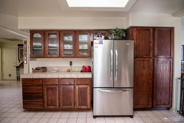 kitchen with a skylight, glass insert cabinets, light countertops, and freestanding refrigerator