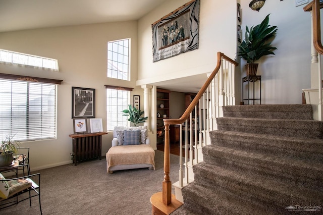 interior space with a high ceiling, carpet flooring, baseboards, radiator heating unit, and ornate columns