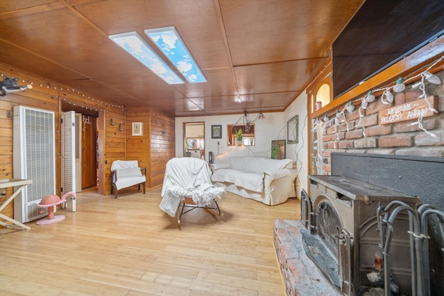 bedroom featuring wooden walls, a skylight, light hardwood / wood-style floors, and a wood stove