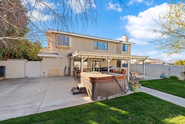 back of property featuring a hot tub, a lawn, a patio, a gate, and stucco siding