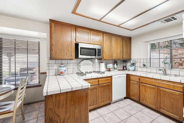 kitchen featuring white appliances, backsplash, a sink, and brown cabinets