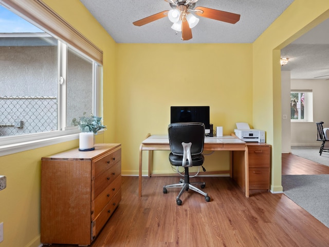 home office with a textured ceiling, a ceiling fan, baseboards, and wood finished floors