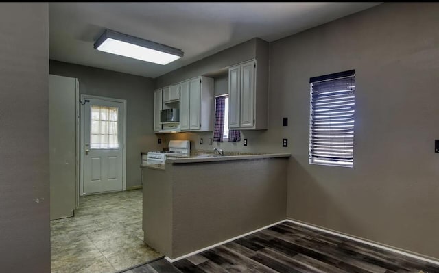 kitchen with kitchen peninsula, white cabinetry, hardwood / wood-style floors, and white gas range oven