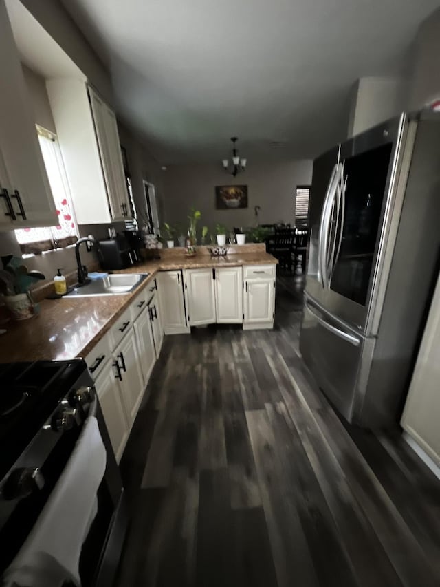 kitchen with stove, sink, stainless steel fridge, a notable chandelier, and white cabinetry