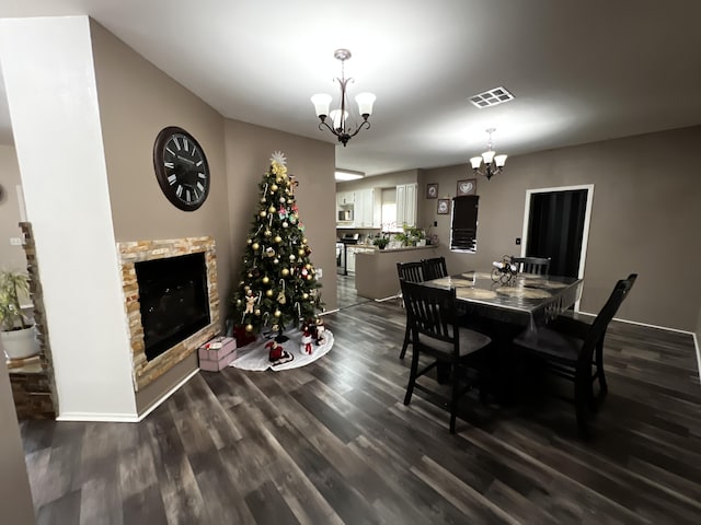 dining space featuring dark wood-type flooring, an inviting chandelier, and a stone fireplace