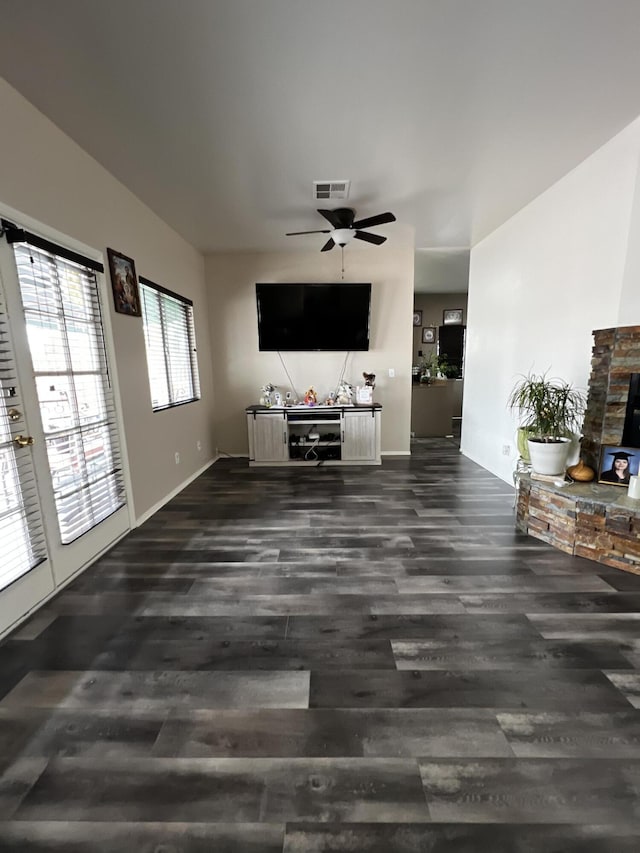 unfurnished living room featuring a stone fireplace, ceiling fan, and dark wood-type flooring