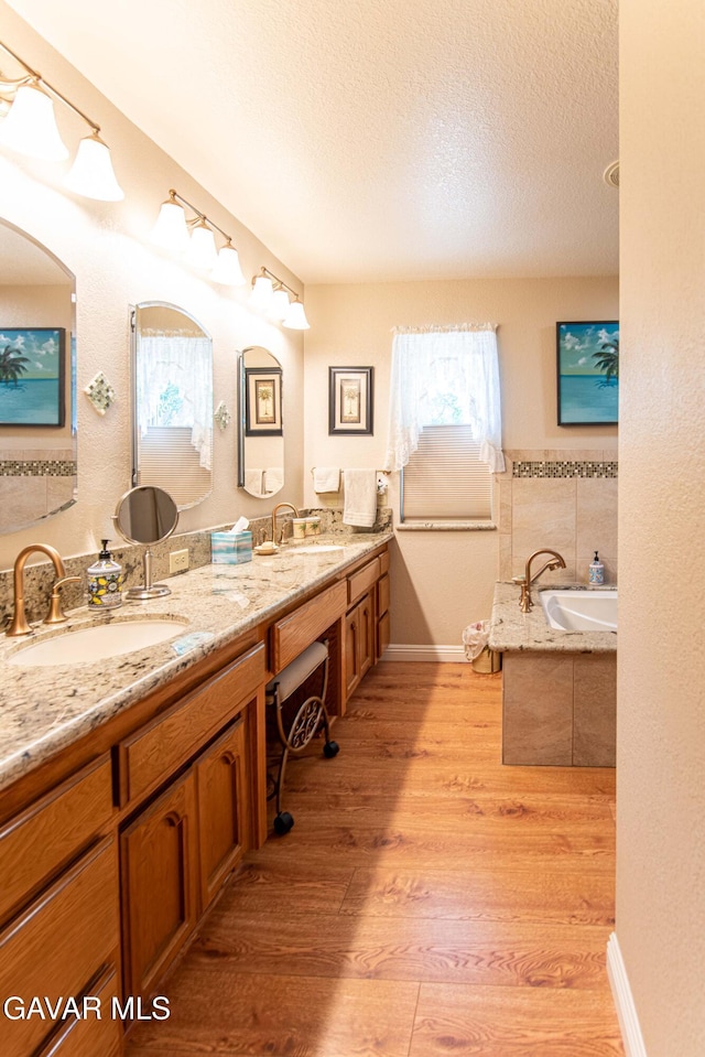 43710 Shiloh Ln, Lancaster, CA 93535 - bathroom featuring double vanity, plenty of natural light, a garden tub, wood finished floors, and a textured ceiling