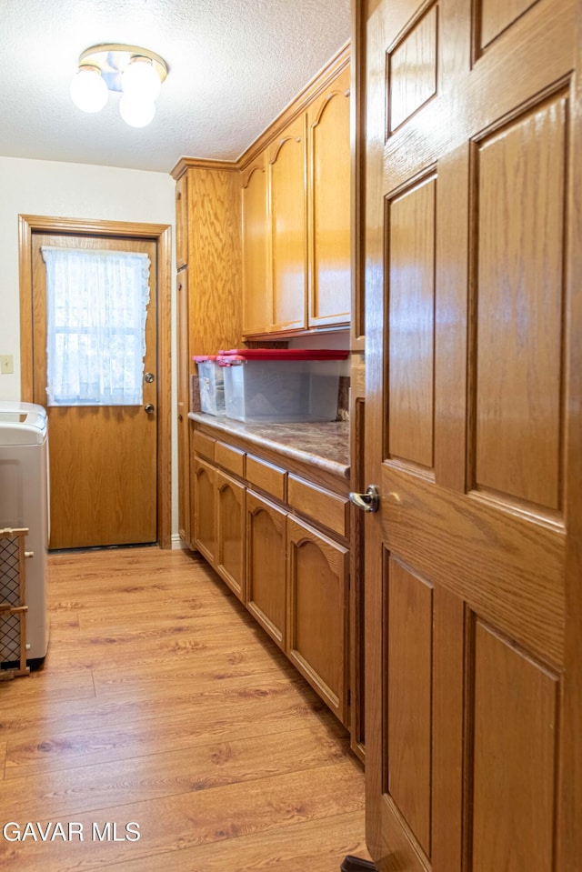 43710 Shiloh Ln, Lancaster, CA 93535 - kitchen with washer / dryer, light wood-style flooring, brown cabinetry, light countertops, and a textured ceiling