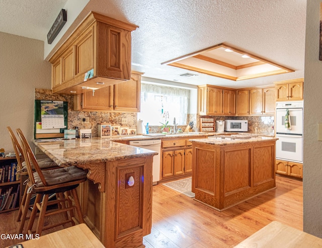 43710 Shiloh Ln, Lancaster, CA 93535 - kitchen with white appliances, a textured ceiling, a peninsula, light wood-style floors, and backsplash