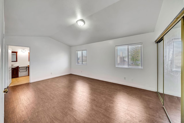 unfurnished bedroom with multiple windows, ensuite bath, a closet, and lofted ceiling