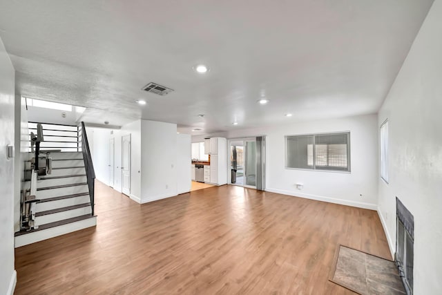 unfurnished living room with a tiled fireplace, a wealth of natural light, and light wood-type flooring