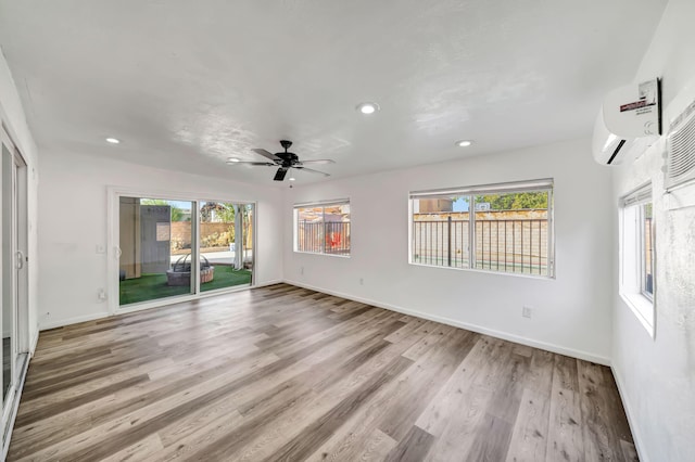 unfurnished room with a wall mounted air conditioner, ceiling fan, and light hardwood / wood-style flooring