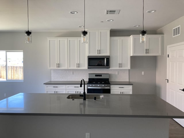 kitchen with appliances with stainless steel finishes, decorative light fixtures, sink, and a center island with sink