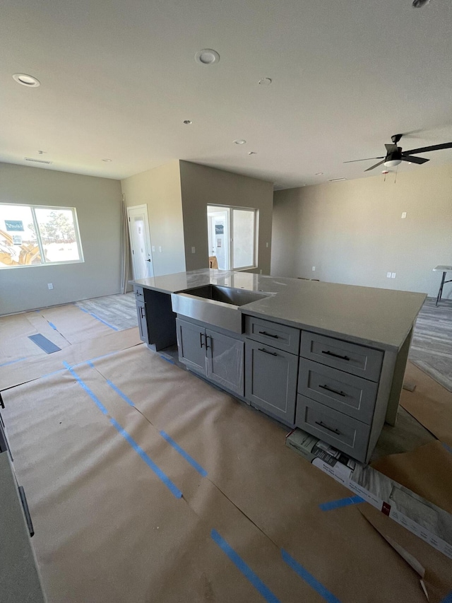 kitchen with ceiling fan, sink, a center island with sink, and gray cabinetry