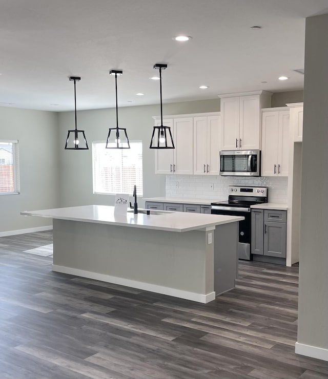 kitchen with white cabinetry, decorative light fixtures, stainless steel appliances, and an island with sink