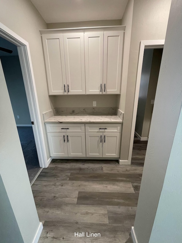 bar with light stone counters, dark wood-type flooring, and white cabinets