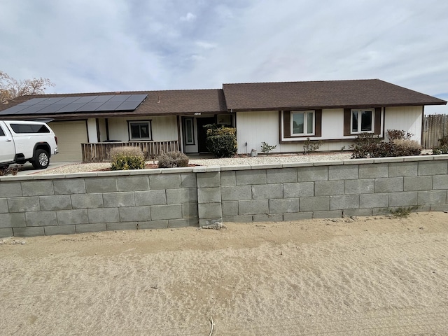 single story home with a garage, concrete driveway, a shingled roof, and solar panels