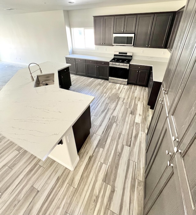 kitchen with light stone countertops, sink, stainless steel appliances, and light wood-type flooring